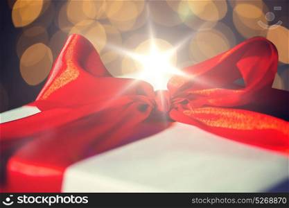 christmas, holidays, presents, new year and celebration concept - close up of gift with red bow over lights background. close up of christmas gift with bow over lights