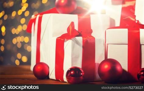 christmas, holidays, presents, new year and celebration concept - close up of gift boxes and red balls on wooden floor over lights background. gift boxes and red balls on wooden floor