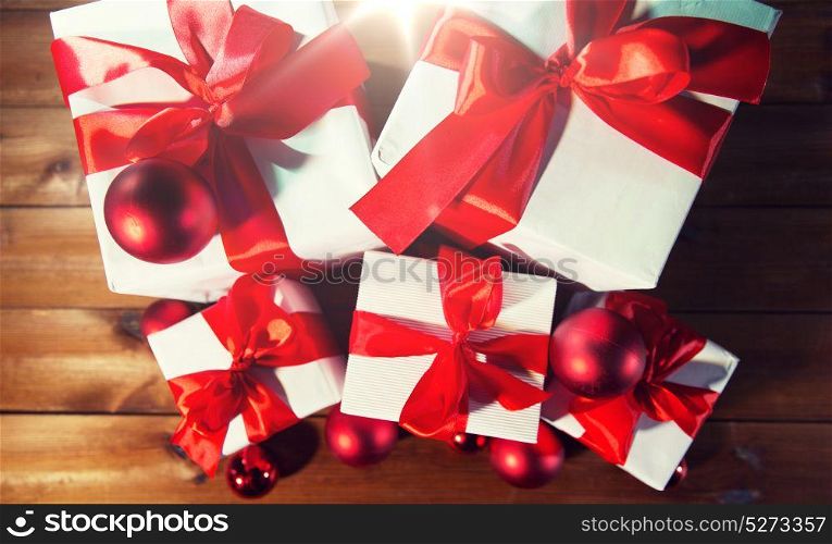 christmas, holidays, presents, new year and celebration concept - close up of gift boxes and red balls on wooden floor from top. close up of gift boxes and red christmas balls
