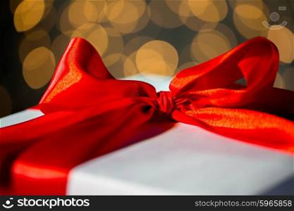 christmas, holidays, presents, new year and celebration concept - close up of gift with red bow over lights background