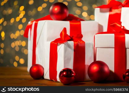 christmas, holidays, presents, new year and celebration concept - close up of gift boxes and red balls on wooden floor over lights background
