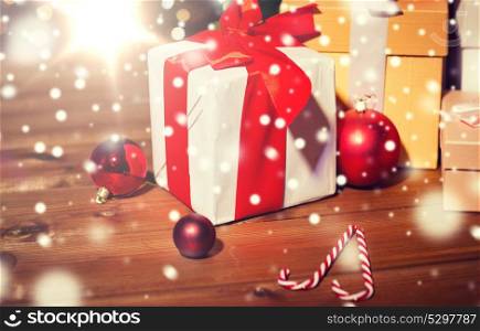 christmas, holidays, presents, new year and celebration concept - group of gift boxes and red balls on wooden board over lights. gifts, candies and christmas balls on wooden board