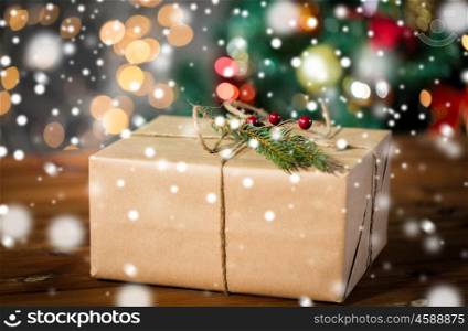 christmas, holidays, presents, new year and decor concept - close up of gift box wrapped into brown mail paper and decorated with fir brunch and rope bow over lights background