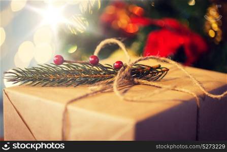 christmas, holidays, presents, new year and decor concept - close up of gift box wrapped into brown mail paper and decorated with fir brunch and rope bow over lights background. close up of christmas gift with fir brunch