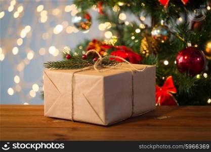 christmas, holidays, presents, new year and decor concept - close up of gift box wrapped into brown mail paper and decorated with fir brunch and rope bow over lights background