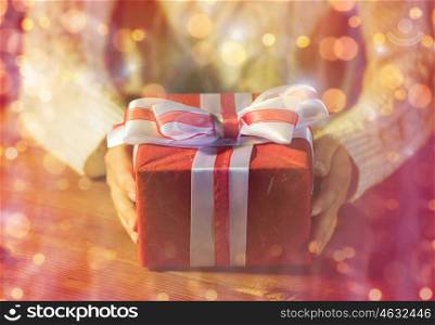 christmas, holidays, presents, new year and people concept - close up of woman hands holding gift box decorated with bow over lights