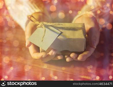 christmas, holidays, presents, new year and people concept - close up of woman hands holding gift box or parcel wrapped into brown mail paper with greeting card over lights