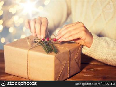 christmas, holidays, presents, new year and people concept - close up of woman decorating gift box or parcel wrapped into brown mail paper with fir brunch. close up of woman with christmas gift or parcel