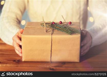 christmas, holidays, presents, new year and people concept - close up of woman with gift box or parcel wrapped into brown mail paper and decorated with fir brunch. close up of woman with christmas gift or parcel