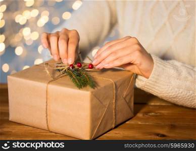 christmas, holidays, presents, new year and people concept - close up of woman decorating gift box or parcel wrapped into brown mail paper with fir brunch