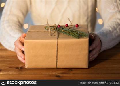 christmas, holidays, presents, new year and people concept - close up of woman with gift box or parcel wrapped into brown mail paper and decorated with fir brunch