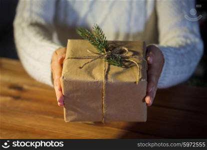 christmas, holidays, presents, new year and people concept - close up of woman hands holding gift box or parcel wrapped into brown mail paper and decorated with fir brunch