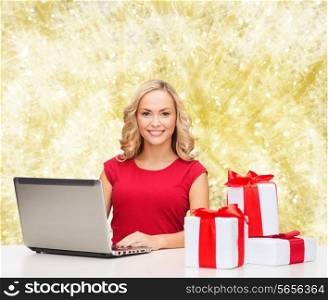 christmas, holidays, technology, advertising and people concept - smiling woman in red blank shirt with gifts and laptop computer over yellow lights background