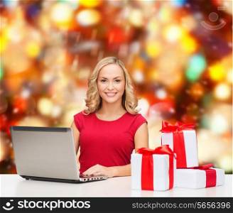 christmas, holidays, technology, advertising and people concept - smiling woman in red blank shirt with gifts and laptop computer over red lights background