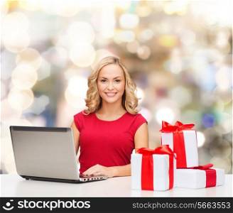 christmas, holidays, technology, advertising and people concept - smiling woman in red blank shirt with gifts and laptop computer over lights background