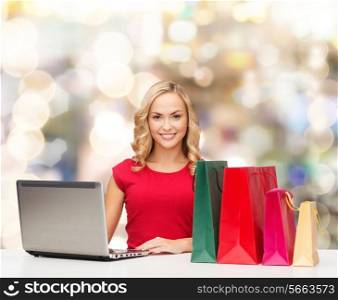 christmas, holidays, technology, advertising and people concept - smiling woman in red blank shirt with shopping bags and laptop computer over lights background