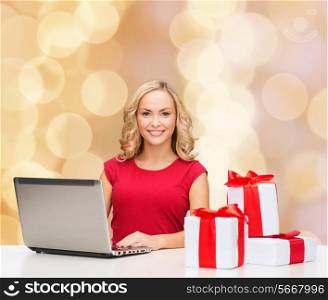 christmas, holidays, technology, advertising and people concept - smiling woman in red blank shirt with gifts and laptop computer over beige lights background
