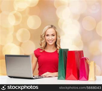 christmas, holidays, technology, advertising and people concept - smiling woman in red blank shirt with shopping bags and laptop computer over beige lights background