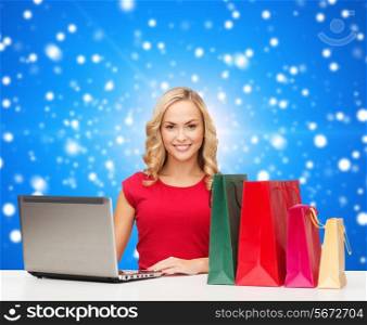 christmas, holidays, technology, advertising and people concept - smiling woman in red blank shirt with shopping bags and laptop computer over blue snowing background
