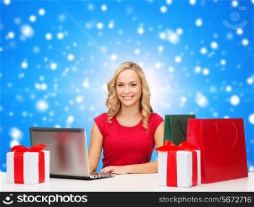 christmas, holidays, technology, advertising and people concept - smiling woman in red blank shirt with shopping bags, gifts and laptop computer over blue snowing background