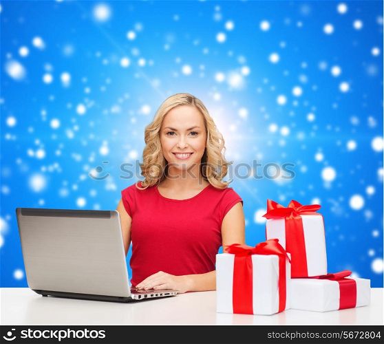 christmas, holidays, technology, advertising and people concept - smiling woman in red blank shirt with gifts and laptop computer over blue snowing background