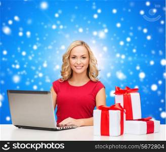christmas, holidays, technology, advertising and people concept - smiling woman in red blank shirt with gifts and laptop computer over blue snowing background