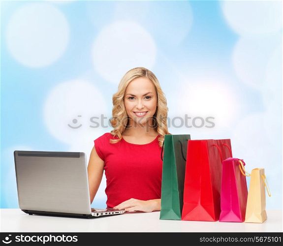 christmas, holidays, technology, advertising and people concept - smiling woman in red blank shirt with shopping bags and laptop computer over blue lights background