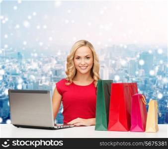 christmas, holidays, technology, advertising and people concept - smiling woman in red blank shirt with shopping bags and laptop computer over snowy city background