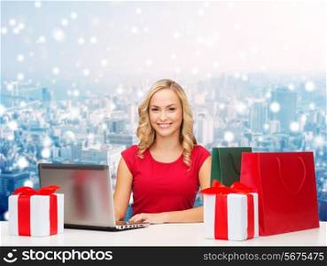 christmas, holidays, technology, advertising and people concept - smiling woman in red blank shirt with shopping bags, gifts and laptop computer over snowy city background