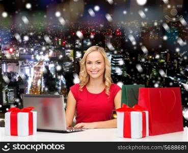 christmas, holidays, technology, advertising and people concept - smiling woman in red blank shirt with shopping bags and laptop computer over snowy city background