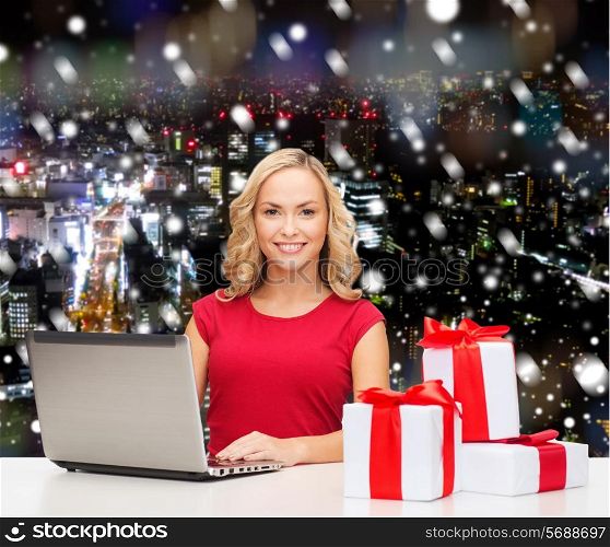 christmas, holidays, technology, advertising and people concept - smiling woman in red blank shirt with gifts and laptop computer over snowy night city background