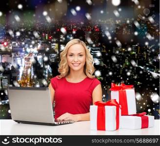 christmas, holidays, technology, advertising and people concept - smiling woman in red blank shirt with gifts and laptop computer over snowy night city background