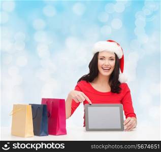 christmas, holidays, technology, advertising and people concept - smiling woman in santa helper hat with shopping bags and tablet pc computer over blue lights background