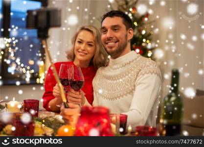 christmas, holidays, technology and people concept - happy couple in taking picture by selfie stick at home dinner over snow. couple taking picture by selfie stick at christmas