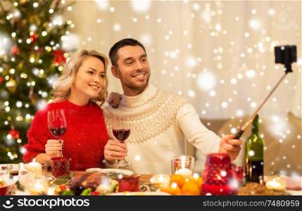 christmas, holidays, technology and people concept - happy couple in taking picture by selfie stick at home dinner over snow. couple taking picture by selfie stick at christmas