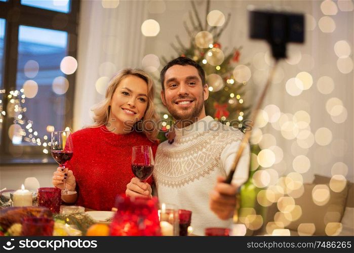 christmas, holidays, technology and people concept - happy couple in taking picture by selfie stick at home dinner. couple taking picture by selfie stick at christmas