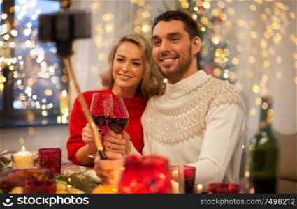 christmas, holidays, technology and people concept - happy couple in taking picture by selfie stick at home dinner. couple taking picture by selfie stick at christmas