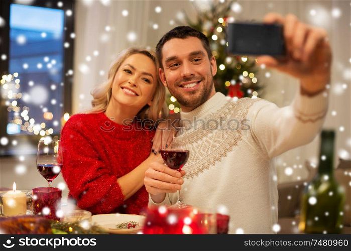 christmas, holidays, technology and people concept - happy couple in taking selfie by smartphone at home dinner over snow. happy couple taking selfie at christmas dinner