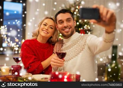 christmas, holidays, technology and people concept - happy couple in taking selfie by smartphone at home dinner over snow. happy couple taking selfie at christmas dinner