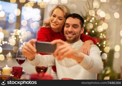 christmas, holidays, technology and people concept - happy couple in taking selfie by smartphone at home dinner. happy couple taking selfie at christmas dinner