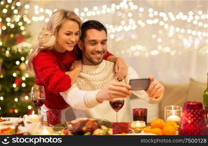 christmas, holidays, technology and people concept - happy couple in taking selfie by smartphone at home dinner. happy couple taking selfie at christmas dinner
