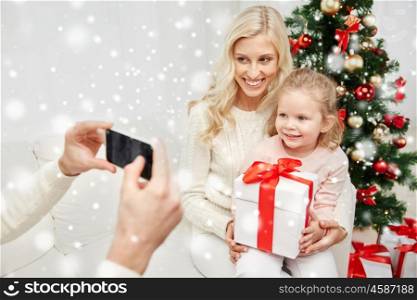 christmas, holidays, technology and people concept - happy family sitting on sofa and taking picture with smartphone at home