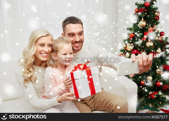 christmas, holidays, technology and people concept - happy family sitting on sofa and taking selfie picture with smartphone at home