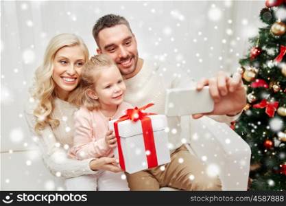 christmas, holidays, technology and people concept - happy family sitting on sofa and taking selfie picture with smartphone at home