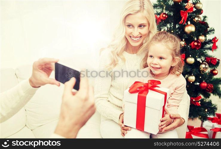 christmas, holidays, technology and people concept - happy family sitting on sofa and taking picture with smartphone at home. family taking picture with smartphone at christmas