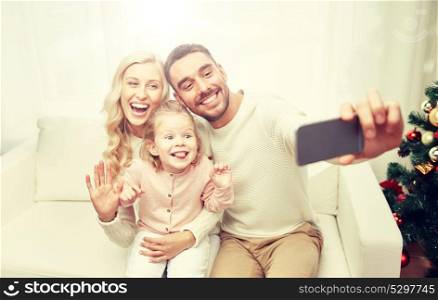 christmas, holidays, technology and people concept - happy family sitting on sofa and taking selfie picture with smartphone at home. family taking selfie with smartphone at christmas