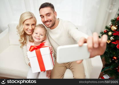 christmas, holidays, technology and people concept - happy family sitting on sofa and taking selfie picture with smartphone at home