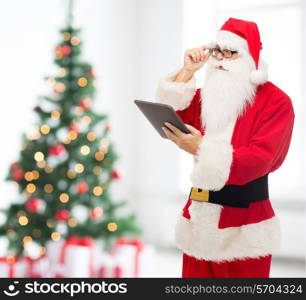 christmas, holidays, technology and people concept - man in costume of santa claus with tablet pc computer over living room and tree background