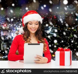 christmas, holidays, technology and people concept - smiling woman in santa helper hat with gift box and tablet pc computer over snowy night city background