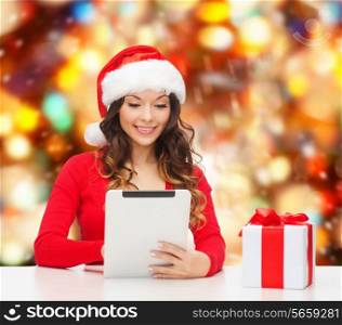 christmas, holidays, technology and people concept - smiling woman in santa helper hat with gift box and tablet pc computer over red lights background
